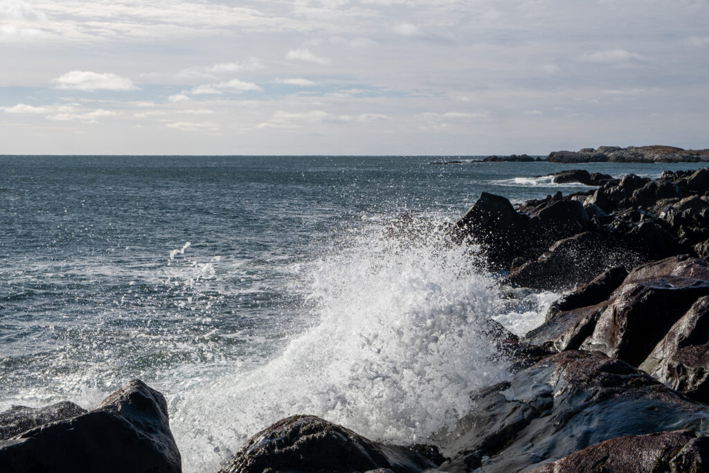 deep blue atlantic ocean crashes in white waves on black rocky shoreline